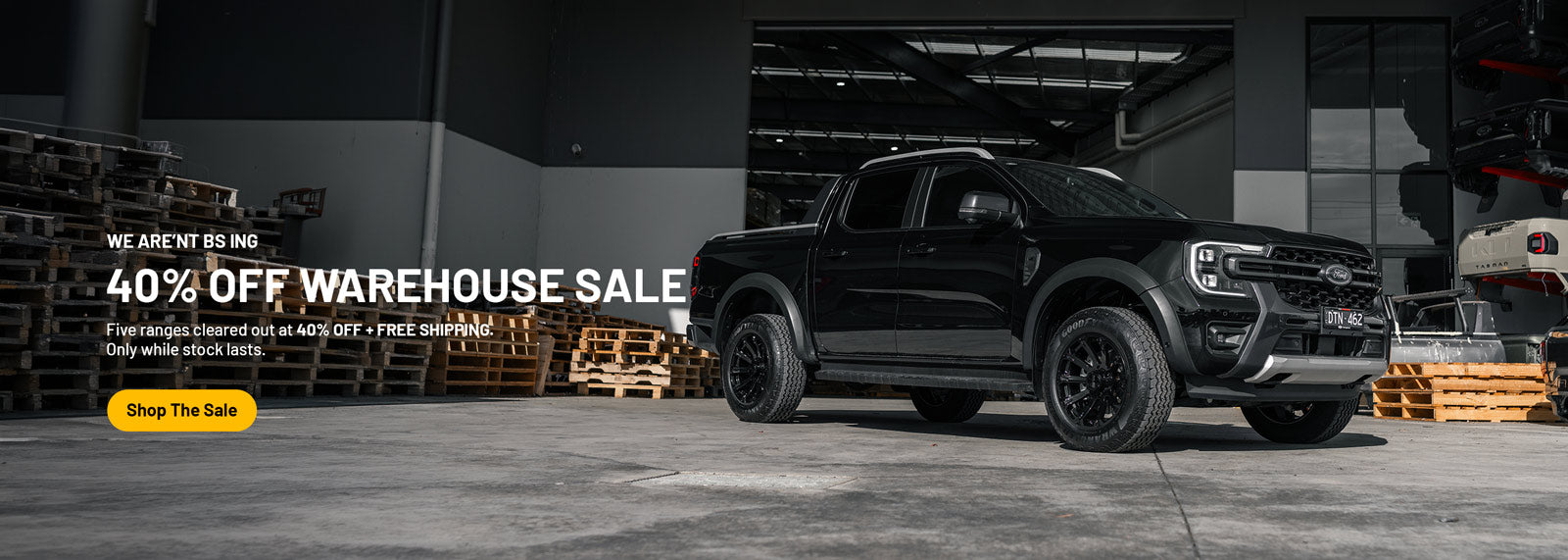 A black Ford Ranger pickup truck parked in a large industrial warehouse setting, with promotional text on the left reading '40% OFF WAREHOUSE SALE' and a yellow 'Shop The Sale' button.