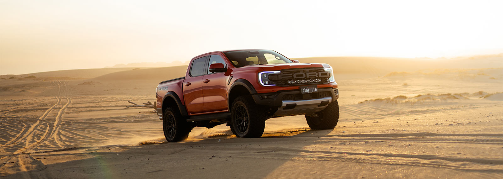 Ford Ranger Raptor pickup truck driving on a desert road with a sunset in the background